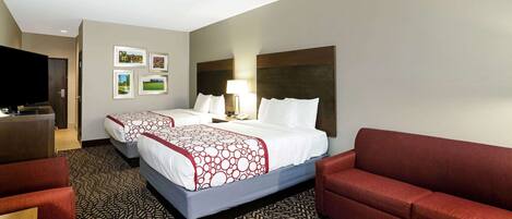 A hotel room with two beds, a desk, a TV, and a red sofa.
