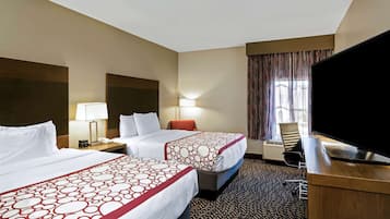 Une chambre d’hôtel avec deux lits, un bureau doté d’un téléviseur à écran plat, une lampe et une fenêtre avec des rideaux.