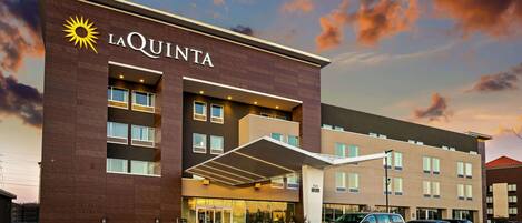 A La Quinta hotel with a modern facade, a covered entrance, and a parking lot with several cars.