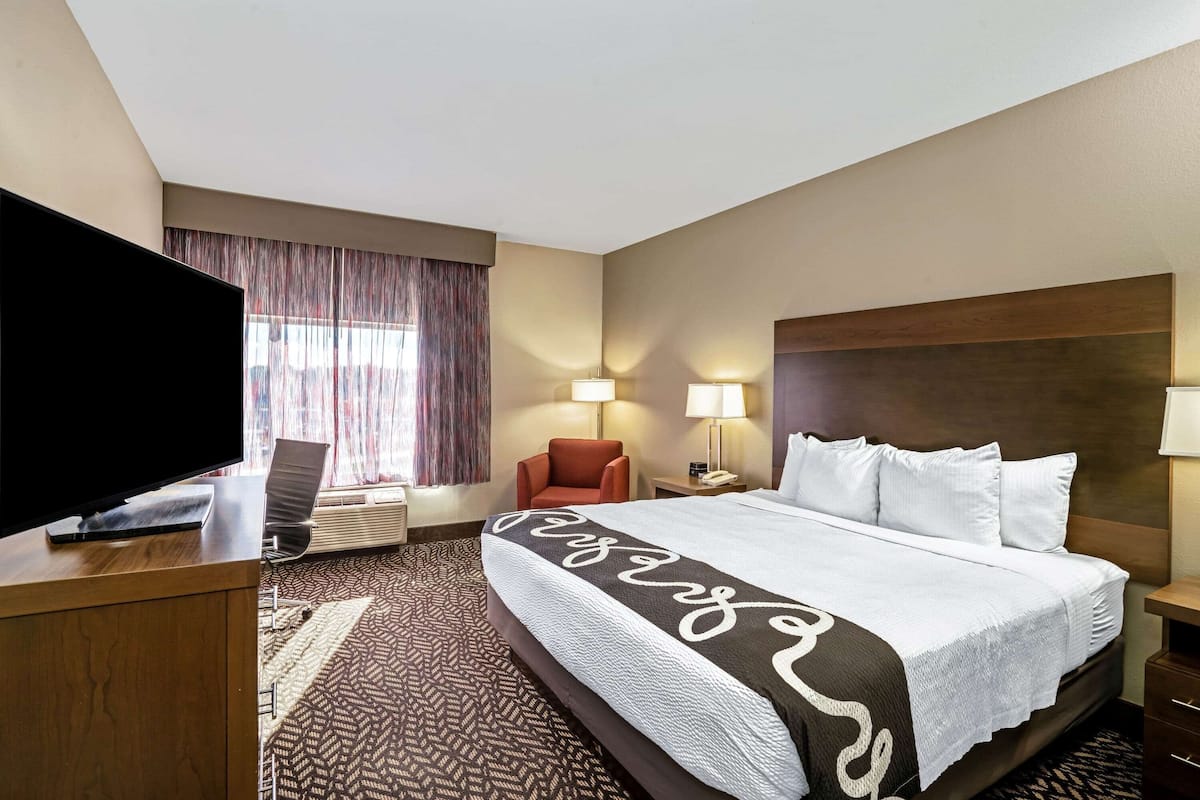 Une chambre d’hôtel dotée d’un grand lit, d’un téléviseur à écran plat, d’un bureau, d’une chaise et d’une fenêtre avec des rideaux.