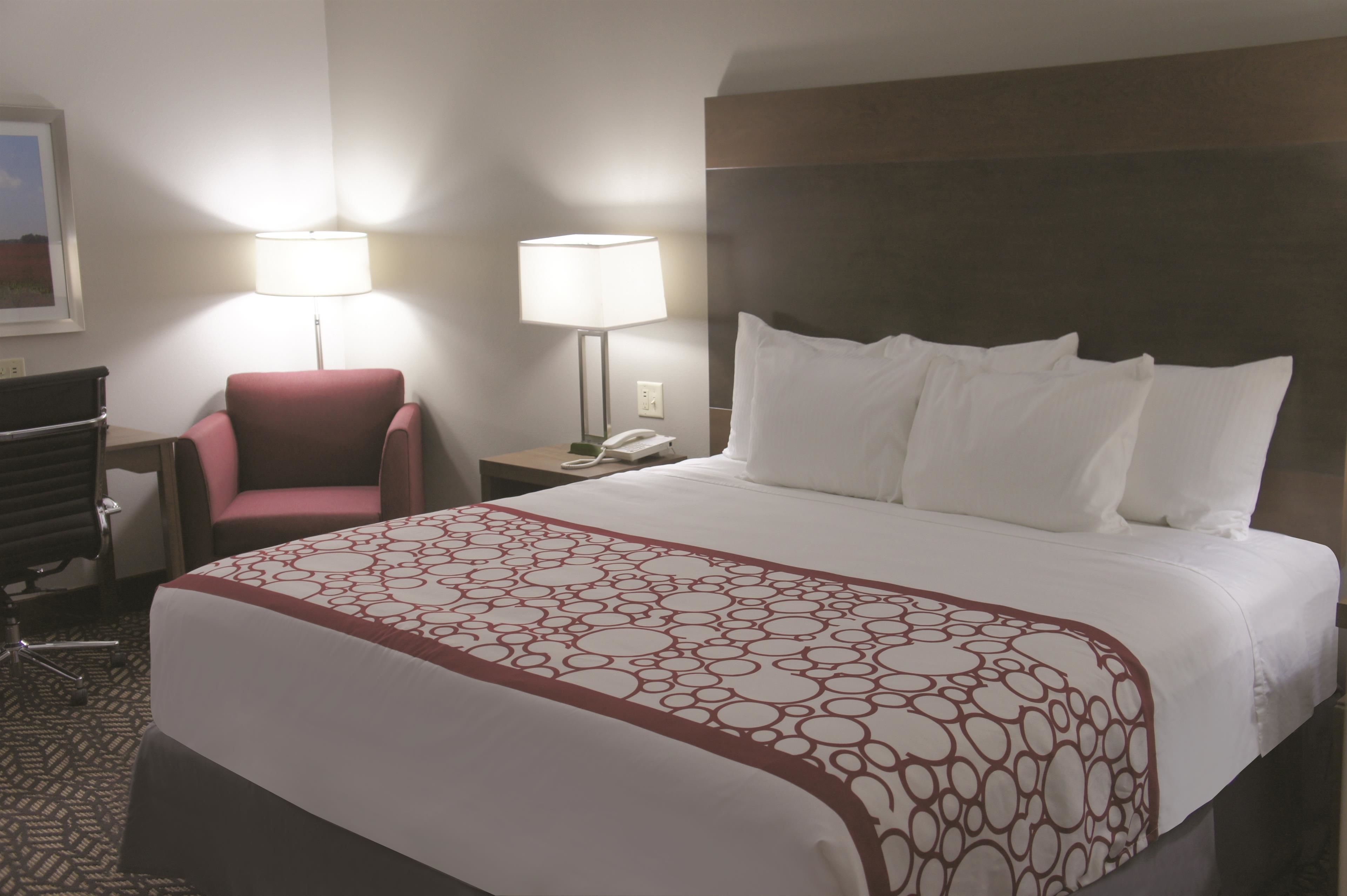 Una habitación de hotel con una cama grande, dos lámparas de noche, un sillón rojo y un escritorio con teléfono.