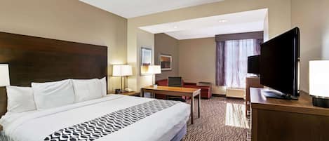 A hotel room with a large bed, a desk, a television, and a window with curtains.