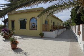 Un bâtiment jaune avec un patio carrelé, une fresque murale et des plantes en pot.
