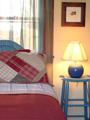 A bed with a red and white checkered blanket, a blue chair, a blue stool, and a lamp. - DeHart Cabin (Lexington)