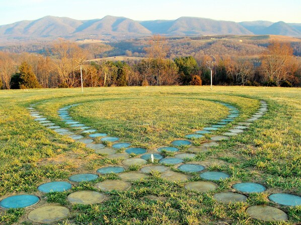 A circular stone pathway in a grassy field with mountains in the background.