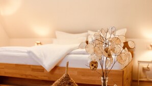 A bedroom with a wooden bed, a round table with a glass vase and a decorative object, and a wall-mounted nightstand. - Zum Alten Backhaus (Burg (Spreewald))