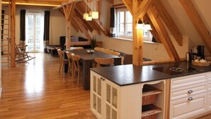 A spacious room with a wooden ceiling, a dining table with chairs, a kitchen area with a sink and cabinets, and a window providing natural light. - Zum Alten Backhaus (Burg (Spreewald))