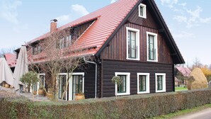 A wooden house with a red roof, white windows, and a garden area with potted plants. - Zum Alten Backhaus (Burg (Spreewald))