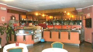 A bar area with shelves of bottles, a counter, and a seating area with tables and chairs. - Hotel Palladio (San Fior di Sopra)
