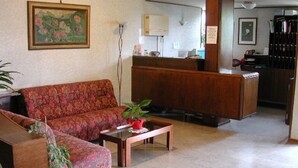 A hotel lobby with a sofa, a coffee table, a reception desk, and a painting on the wall. - Hotel Palladio (San Fior di Sopra)