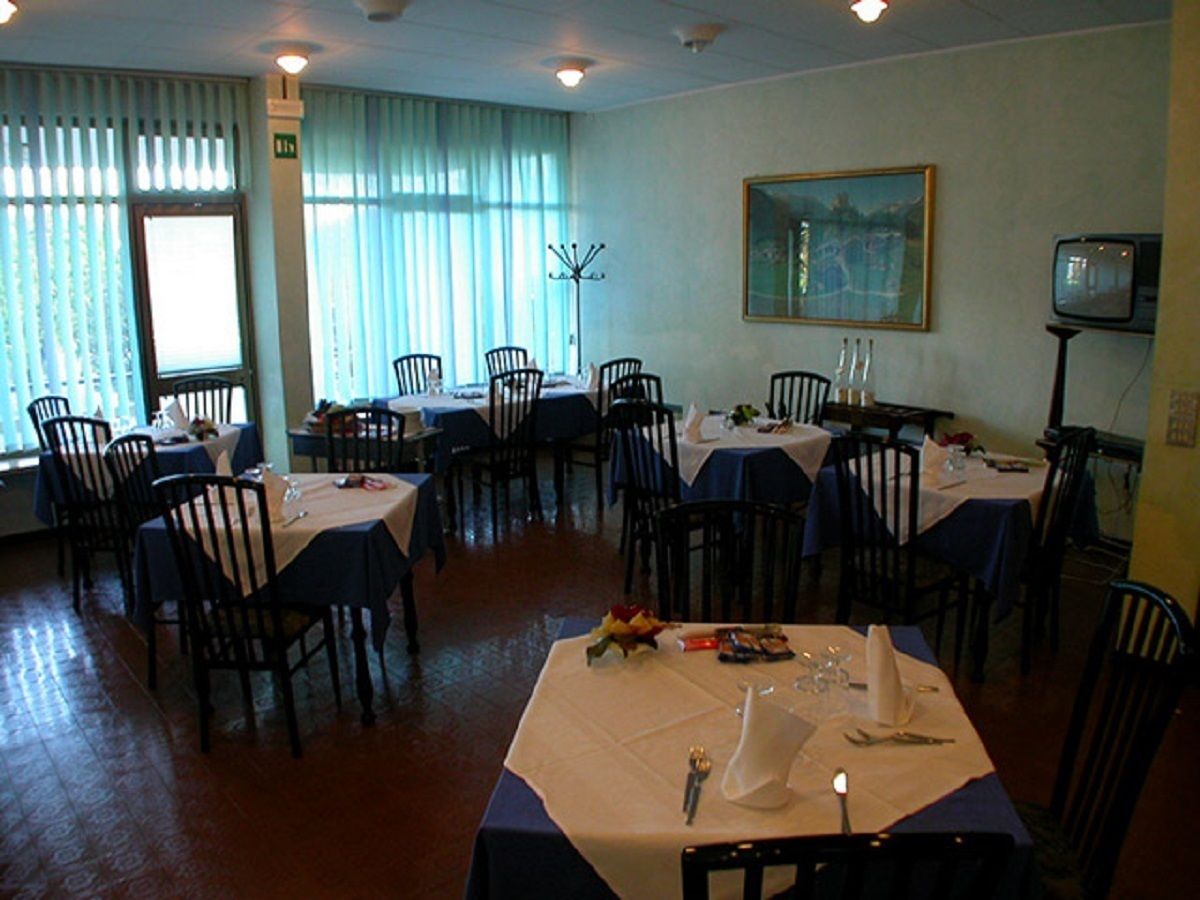 Un espace repas avec plusieurs tables et chaises, un tableau accroché au mur et un téléviseur posé sur un meuble.
