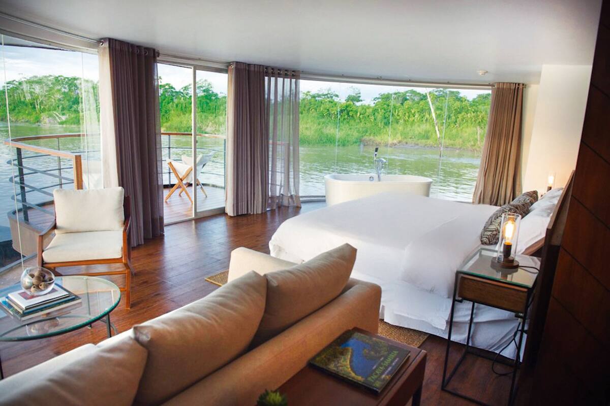 Un dormitorio amplio con una cama grande, una mesa de vidrio, una silla y vistas a un río.