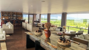 A modern living area with a bar, sofas, and a large glass table with decorative items. - Jungle Experiences Zafiro (Nauta)