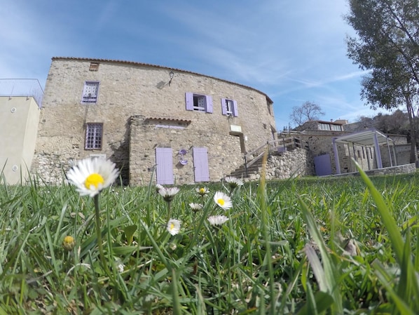 Ein rustikales Steinhaus mit einer Treppe zu einem überdachten Bereich, umgeben von üppiger Vegetation und Blumen.