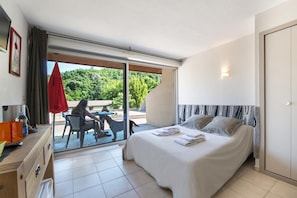 Quarto de hotel com cama, escrivaninha, cadeira e vista para o exterior.
