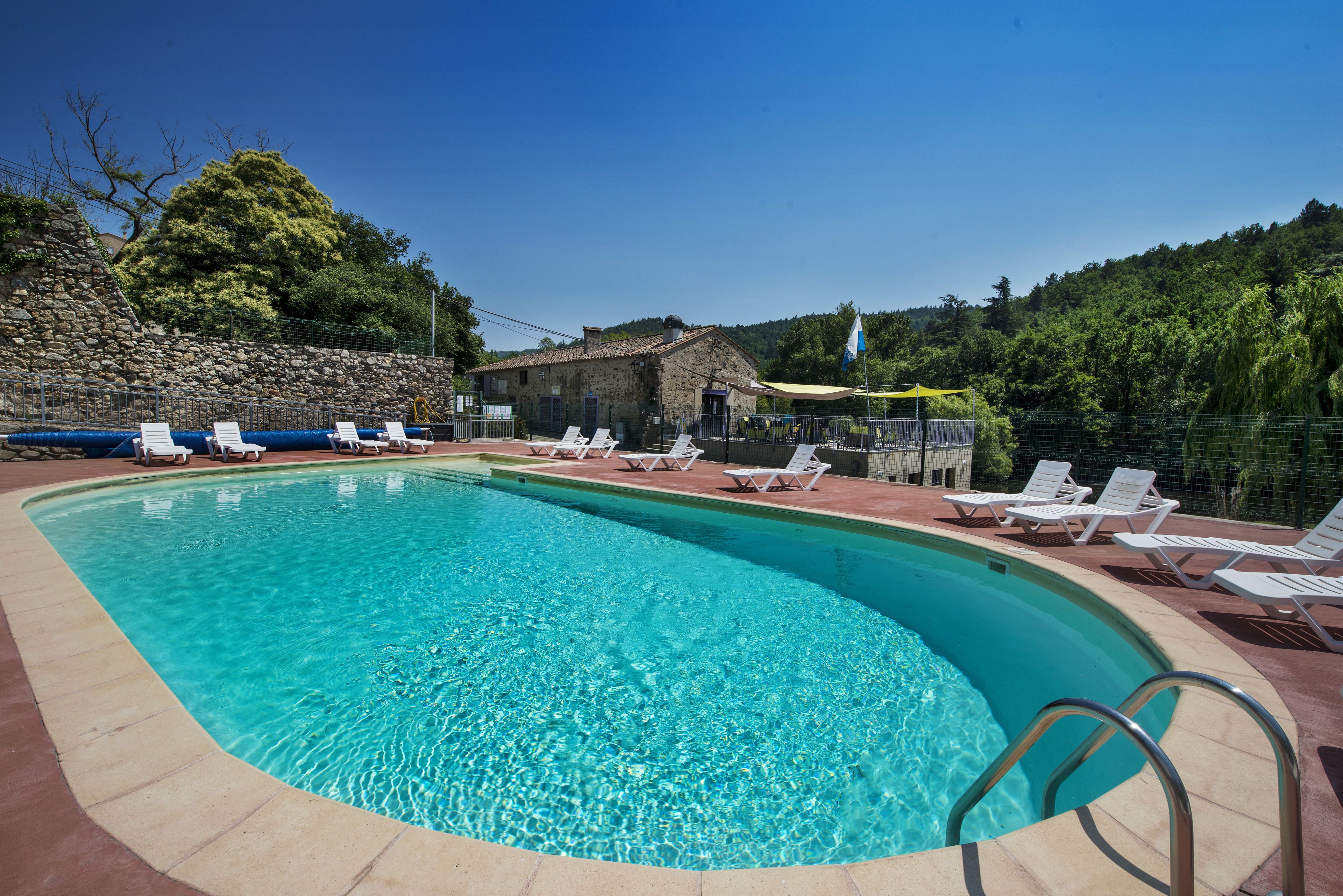 Une piscine avec des chaises longues et, en arrière-plan, un bâtiment en pierre.
