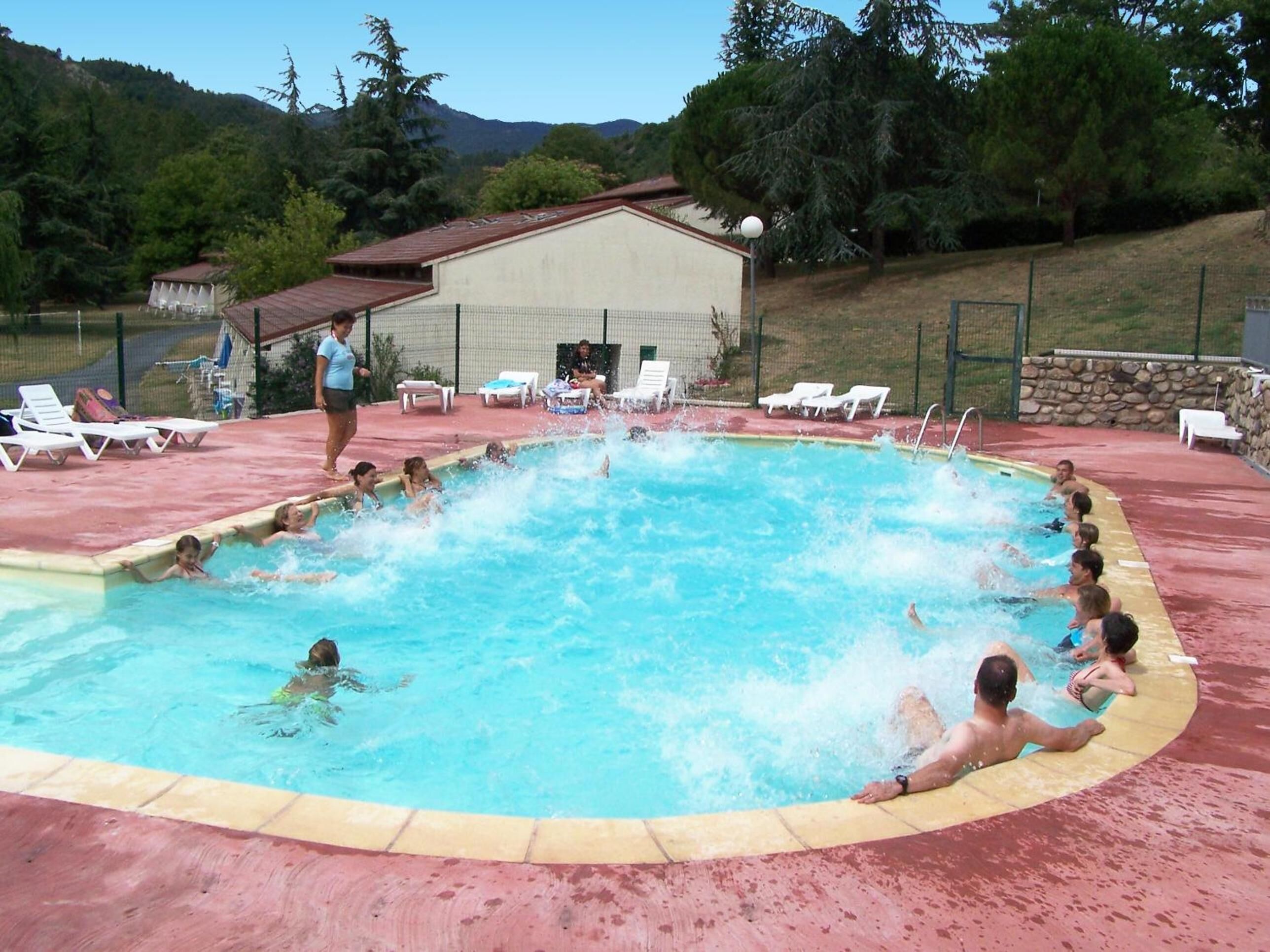 Una piscina con gente, rodeada de sillas de descanso y un edificio al fondo.