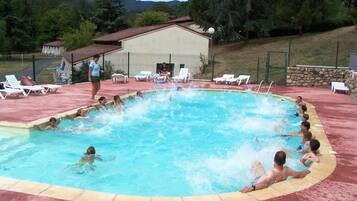 Una piscina con gente, rodeada de sillas de descanso y un edificio al fondo.