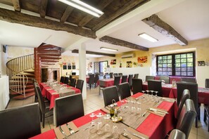 A dining area with multiple tables set for service, a spiral staircase, and a view of the outdoors through a window. - Le Moulin de Sournia - Gites (Sournia)