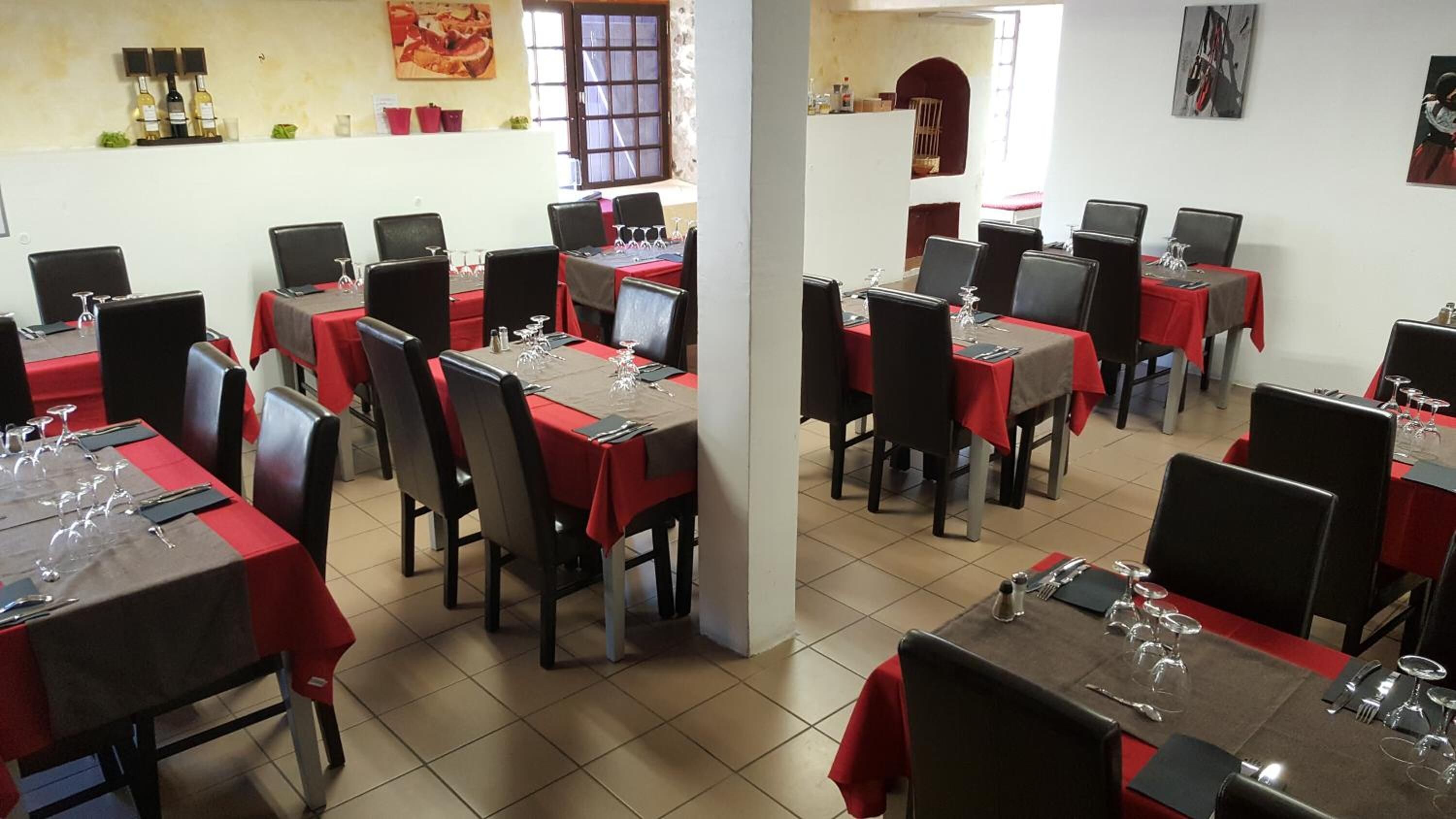 Een restaurant met gedekte tafels, rode tafelkleden en zwarte stoelen.