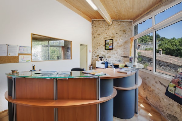 A reception desk with a glass top, wooden panels, and a stone wall backdrop. - Le Moulin de Sournia - Gites (Sournia)