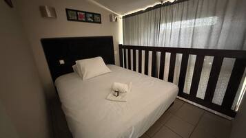 A hotel room with a bed, a headboard, a window with curtains, and a small wall decoration.