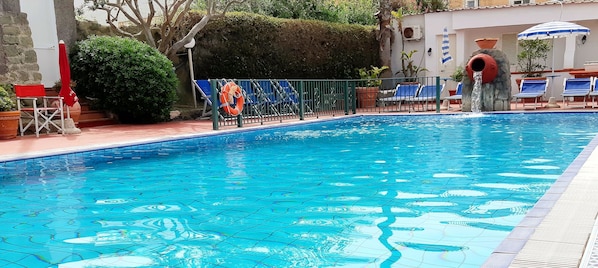 A swimming pool with a tiled floor, surrounded by lounge chairs and a life preserver.