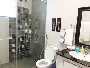 A bathroom with a glass-enclosed shower, a white toilet, a sink with toiletries, and a mirror. - Crystal Cameron Highlands (Tanah Rata)