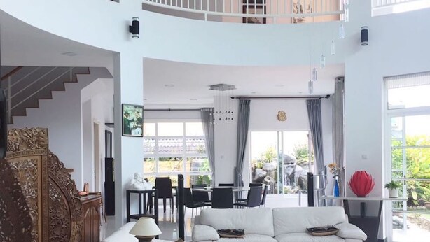A spacious living area with a high ceiling, a staircase, and a balcony.