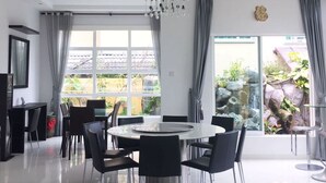A modern dining area with a round table and chairs, large windows with curtains, and a view of a garden.