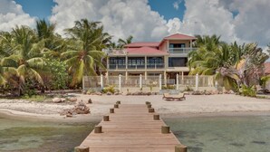 A wooden pier leading to a beachfront property with a two-story building, palm trees, and a sandy beach. - Villa Mission Bay (Placencia)