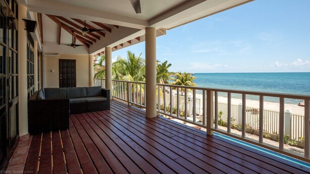 A wooden deck with a sofa, ceiling fans, and a view of the ocean. - Villa Mission Bay (Placencia)