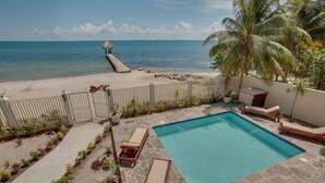 A pool area with lounge chairs, a thatched-roof structure, and a view of the ocean. - Villa Mission Bay (Placencia)