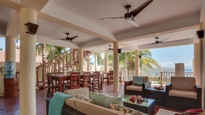 A covered outdoor area with wooden furniture, ceiling fans, and a view of palm trees. - Villa Mission Bay (Placencia)