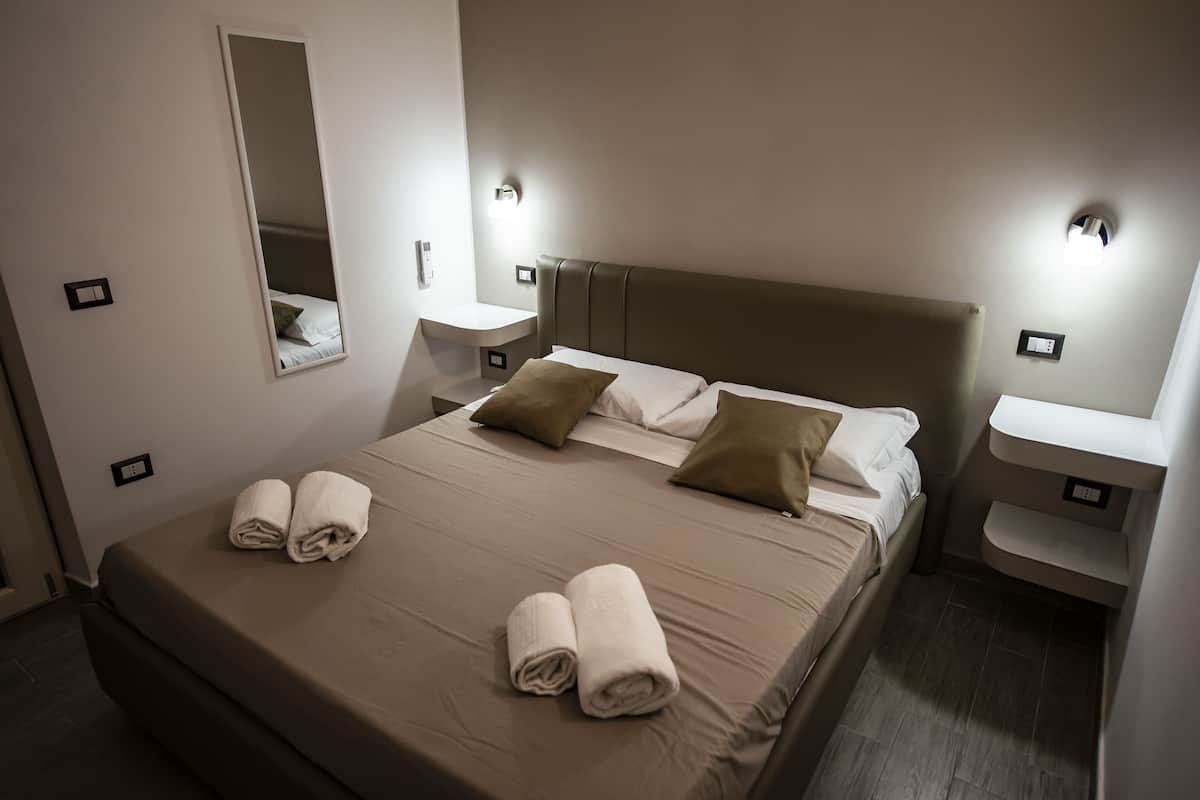 Habitación de hotel con una cama grande, dos mesitas de noche, un espejo y una lámpara fijada a la pared.