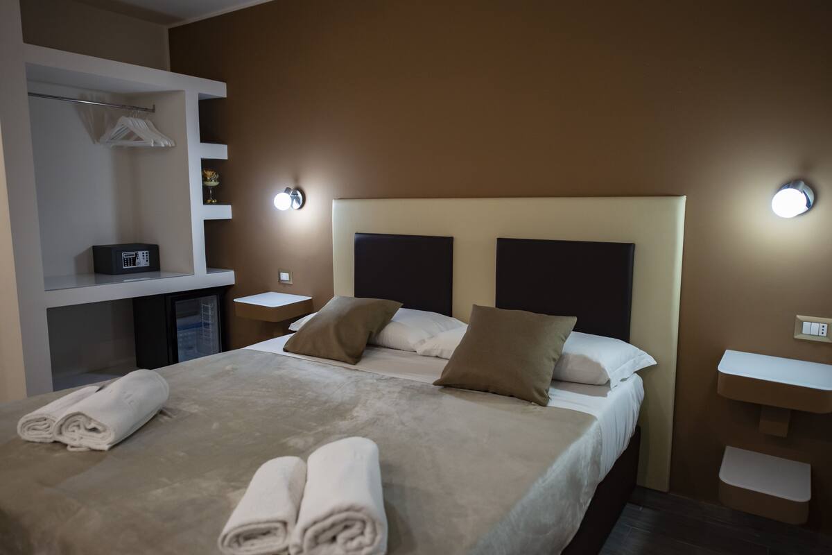 Una habitación de hotel con una cama grande, dos mesitas de noche, un armario y iluminación empotrada.