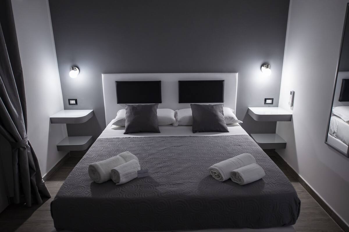 Una habitación de hotel moderna con una cama grande, dos mesitas de noche y un cabecero con iluminación integrada.