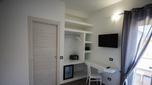 Une chambre moderne dotée d’un bureau intégré, d’un téléviseur fixé au mur et d’un placard à portes coulissantes.