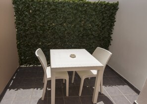A white table and two chairs in a corner with a green hedge wall. - Residenza Magnolia (Tropea)