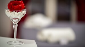 Un bol en verre transparent contenant une rose rouge et des pierres blanches, le tout posé sur une surface réfléchissante.