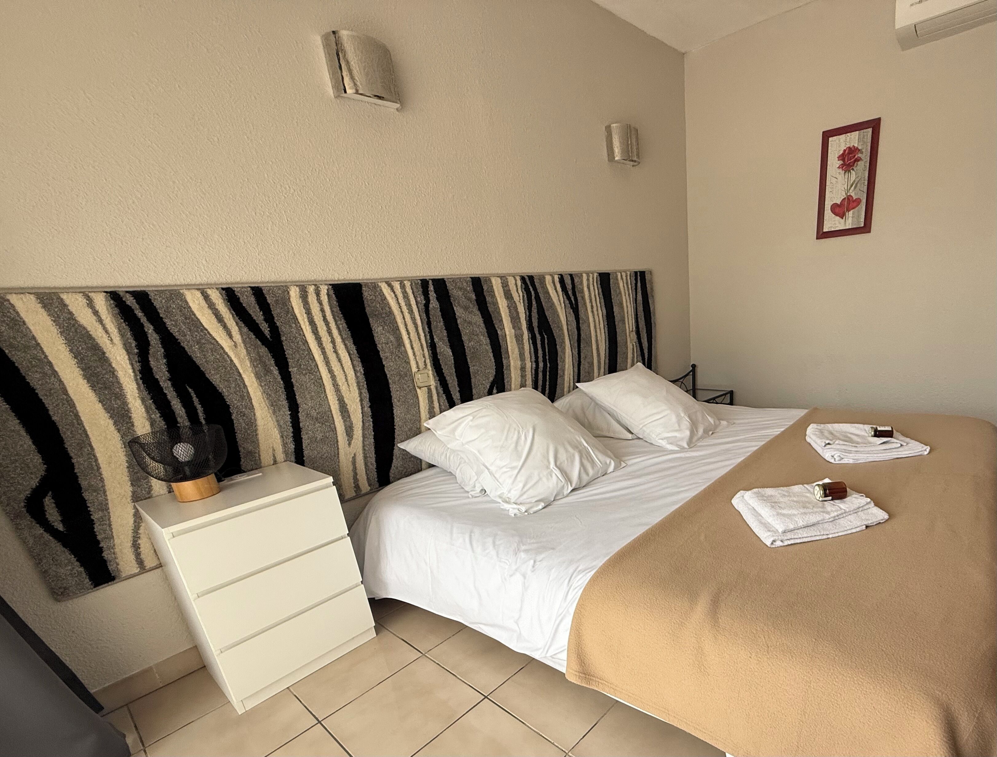 A bed with white bedding, a zebra-striped headboard, a white nightstand, and a beige blanket on the floor.