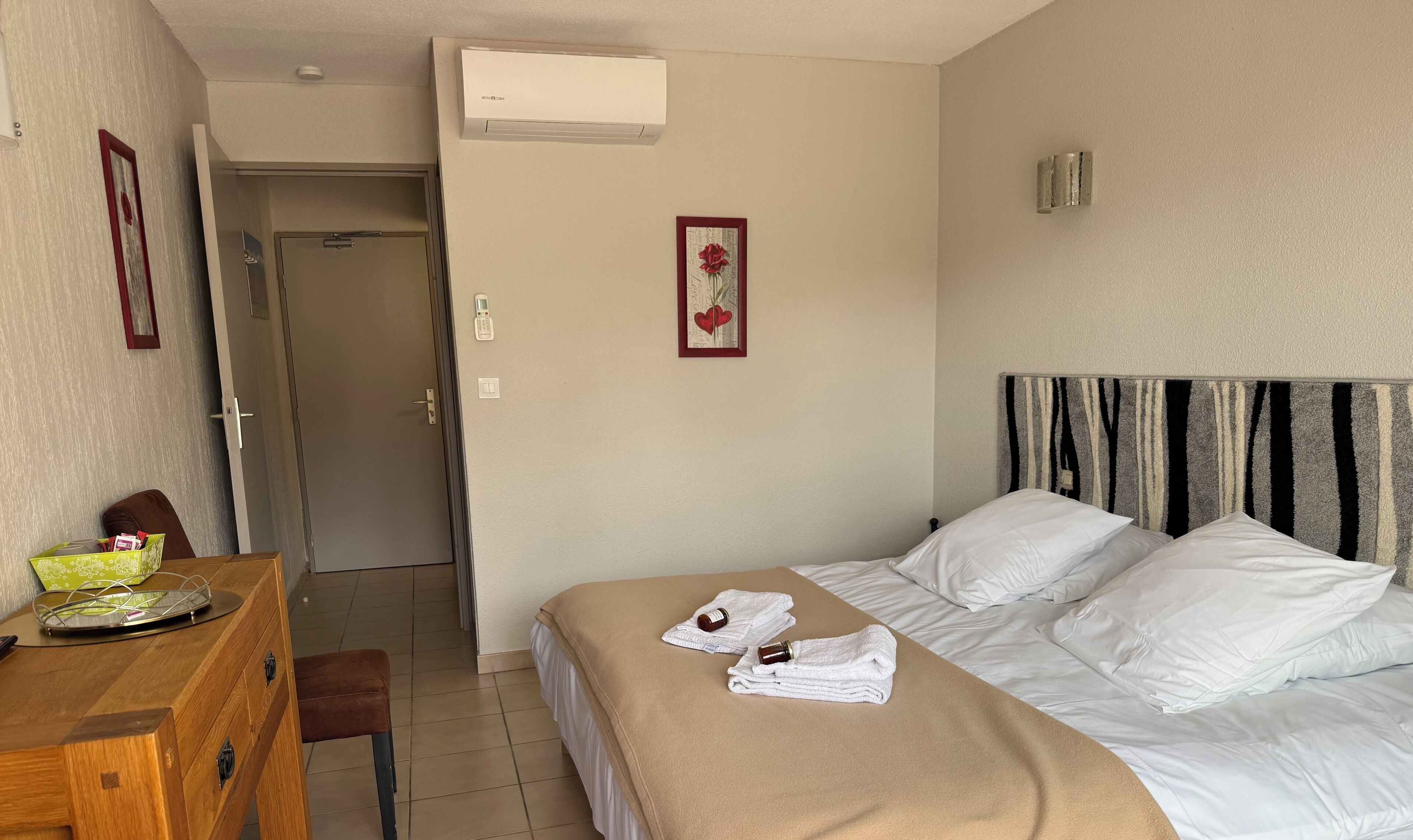 A hotel room with a bed, bedside table, chair, and a door leading to another room.