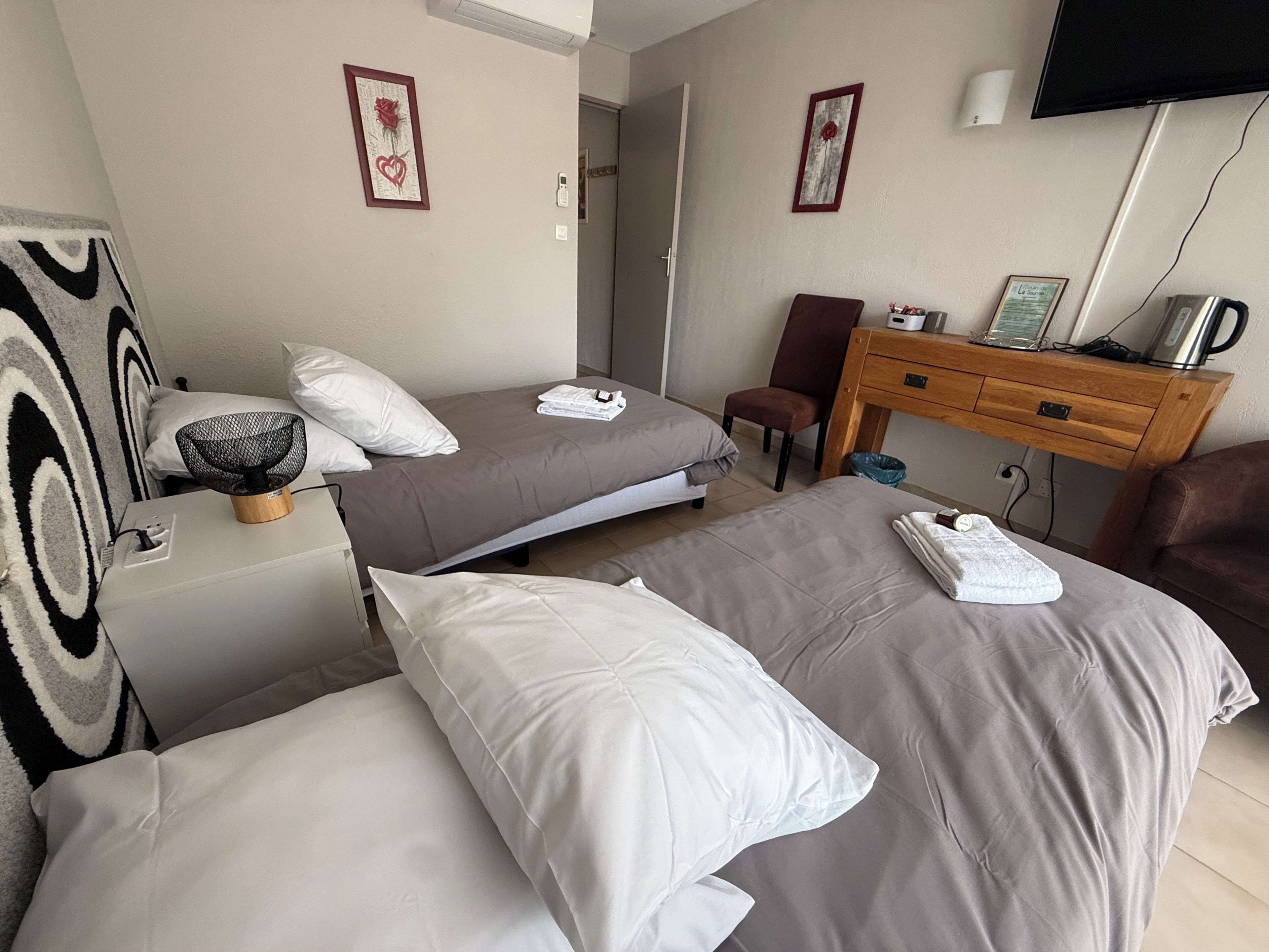 A hotel room with two beds, a desk, a chair, a TV, and artwork on the walls.