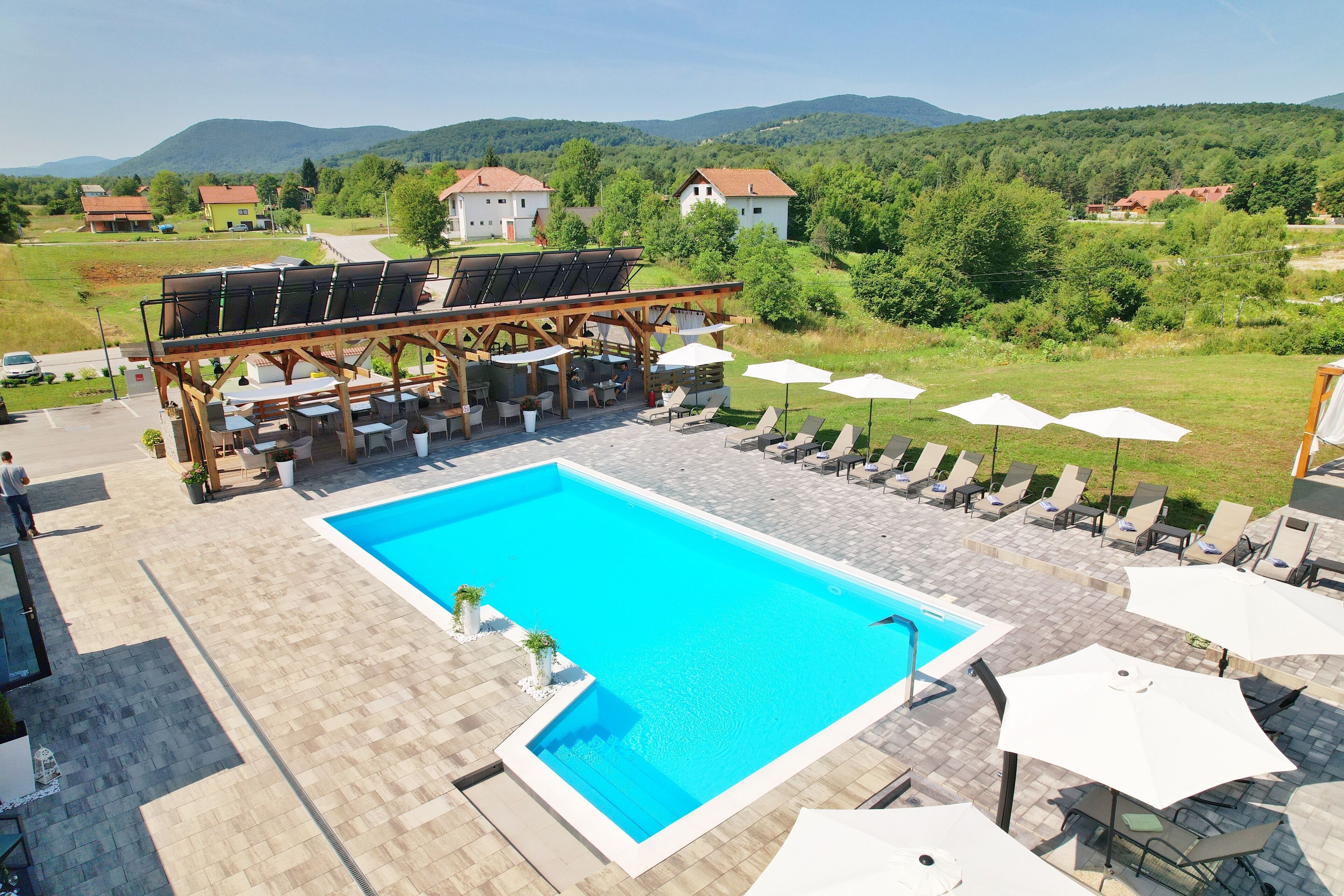 A swimming pool with lounge chairs and umbrellas, surrounded by a wooden deck and a view of the countryside.