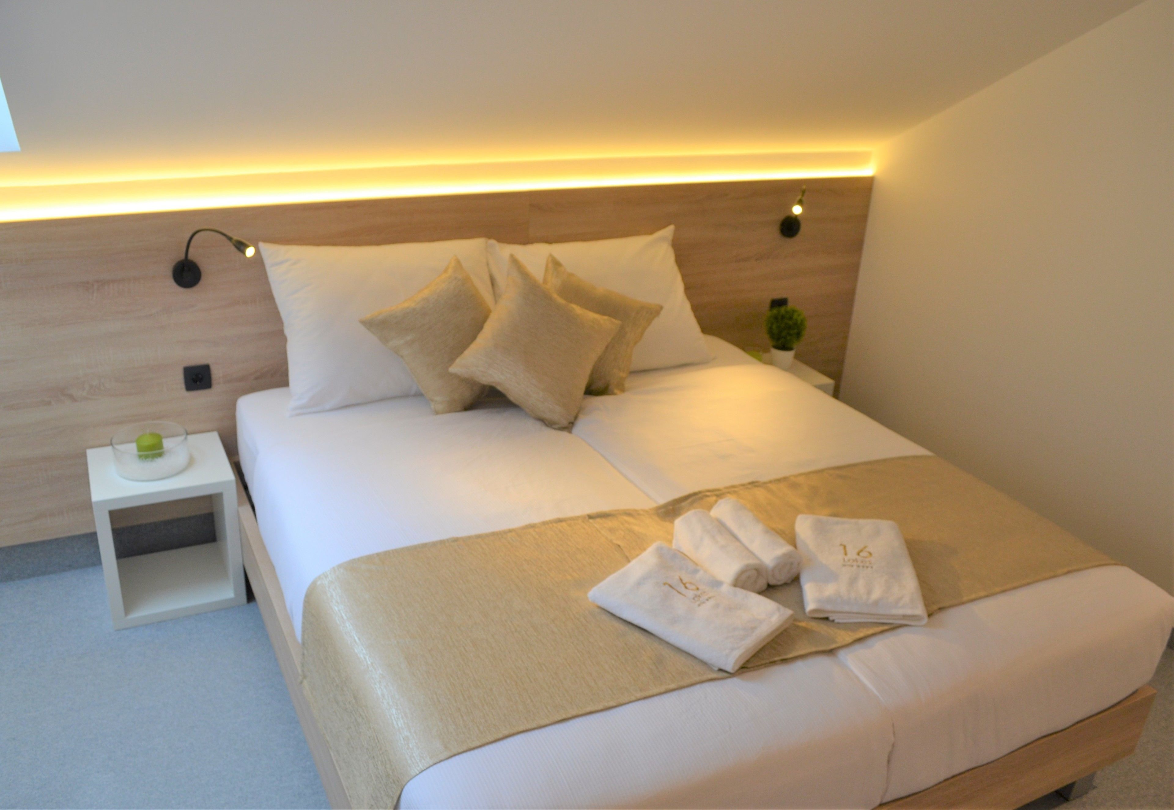 A neatly made bed with a headboard, a bedside table with a lamp, and a small plant.