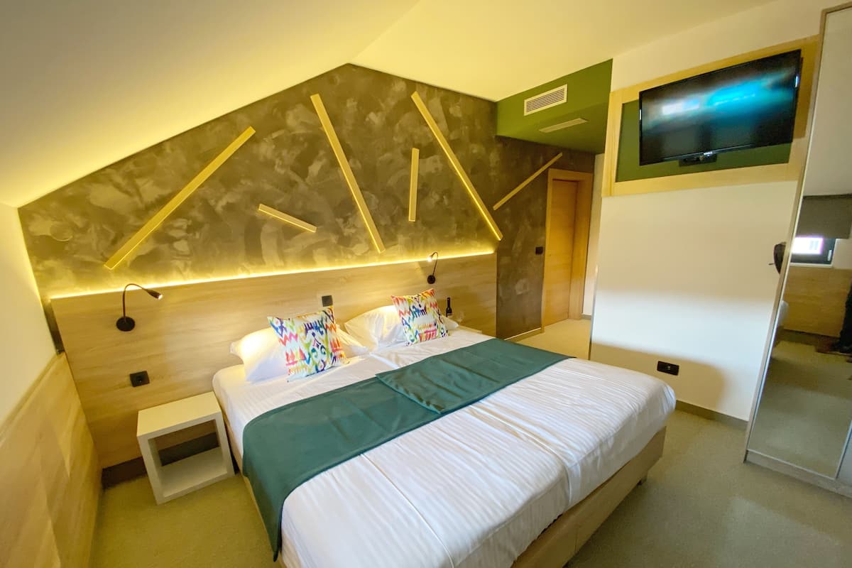 A modern hotel room with a large bed, a TV mounted on the wall, and a unique geometric wall design.