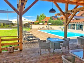 Una terraza de madera con mobiliario exterior, una piscina y vistas a una zona residencial al fondo.