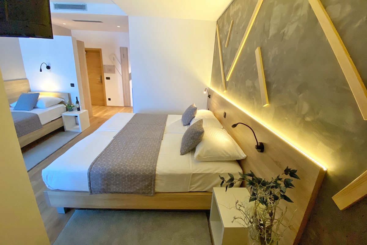 A modern bedroom with a large bed, bedside tables, a wall-mounted light, and a plant.
