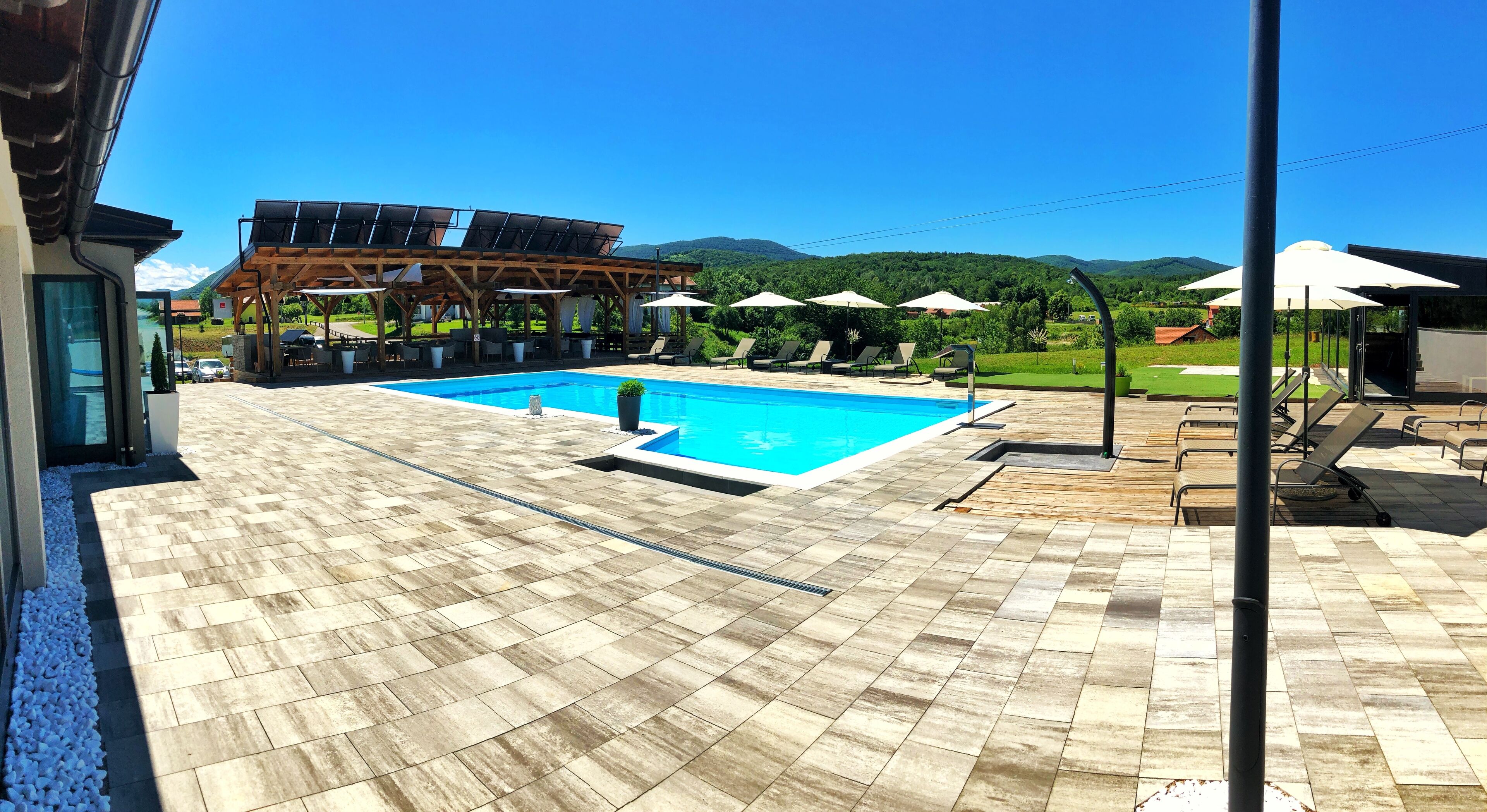 Une piscine avec une terrasse en bois, des chaises longues et des parasols.