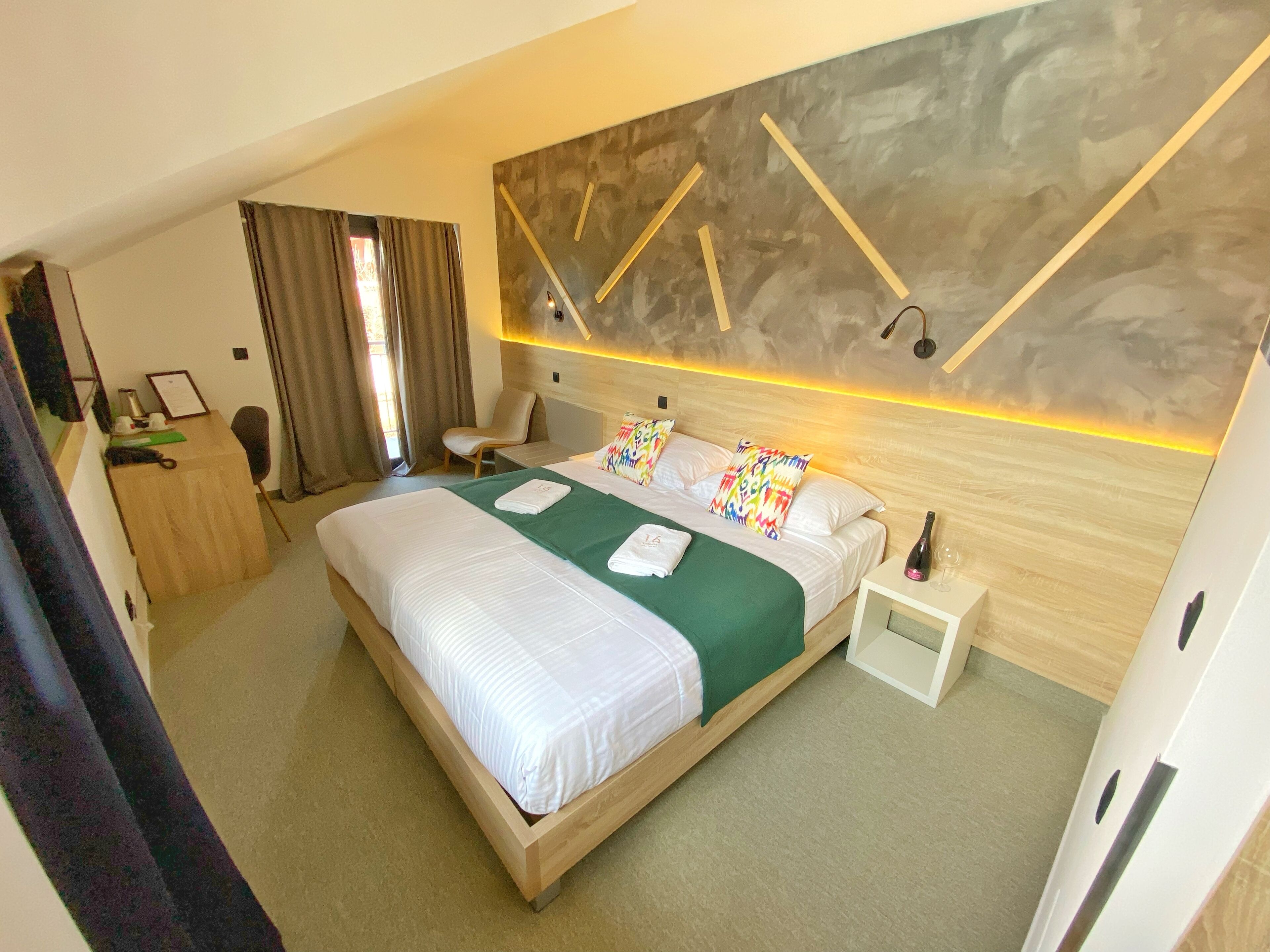 A hotel room with a large bed, a desk, a chair, a nightstand, and a wall with a geometric design.